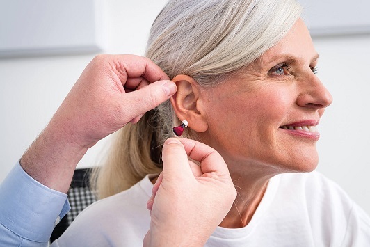 Ältere Frau bekommt modernes Hörgerät vom Akustiker professionell ins Ohr eingesetzt.